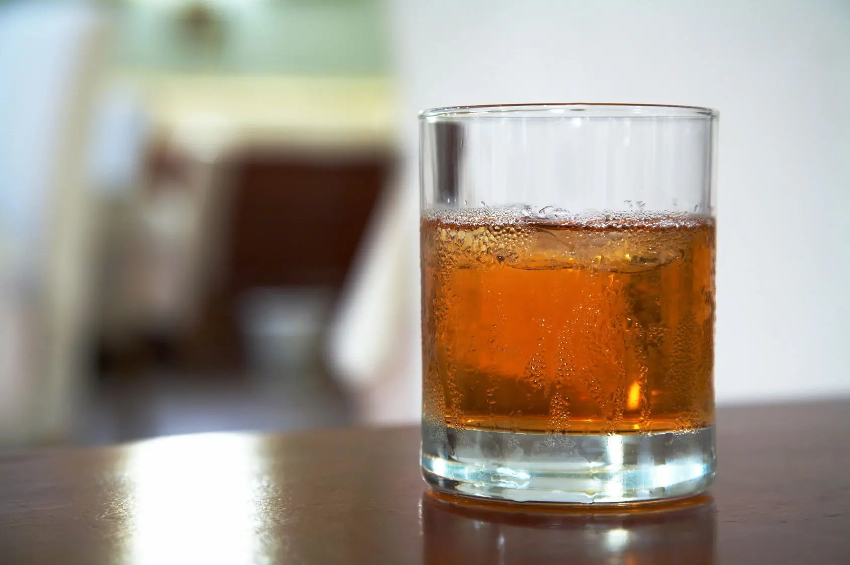A glass of whiskey on a reflective surface with a blurred background.