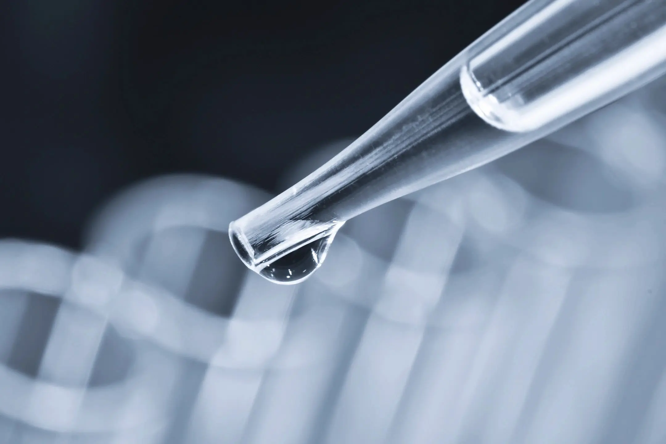 Close-up of a pipette releasing a droplet of clear liquid in a lab.
